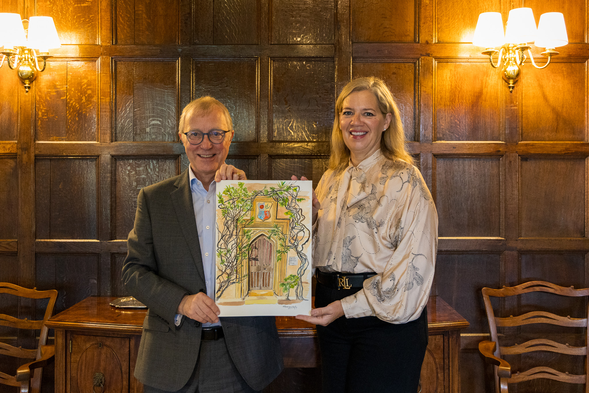 The Master and Simone Desmarchelier holding a painting of the Pembroke SCR entrance by Simone.