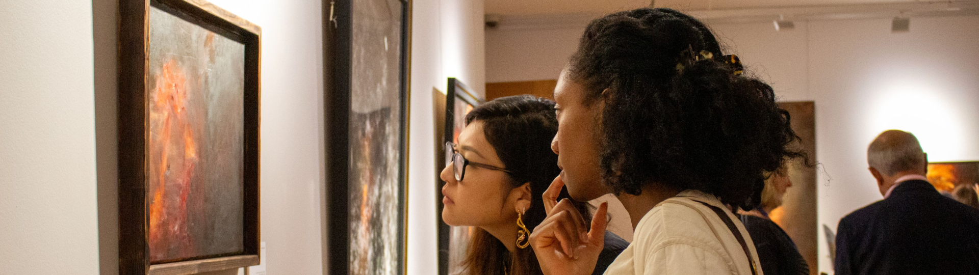 Two students looking at a painting from the Disappearance of Worlds exhibition in the Pembroke JCR Art Gallery.