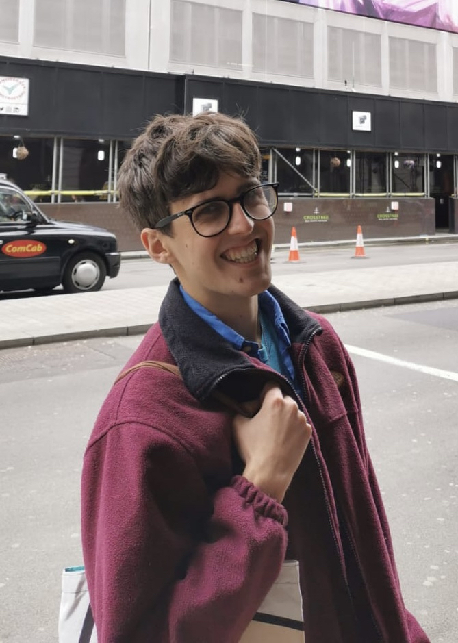 Harrison Kaye, smiling wearing a red jacket and carrying a tote bag