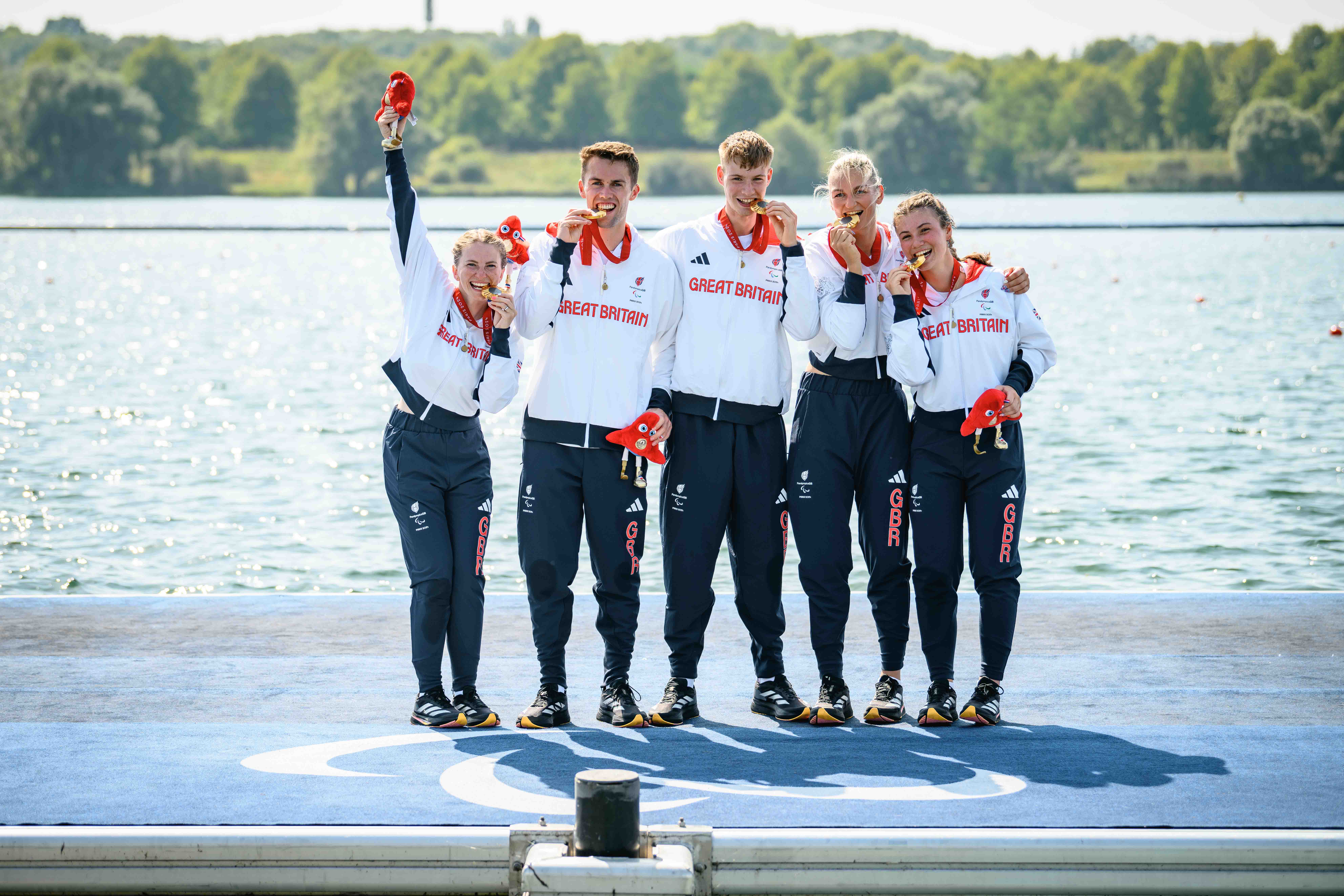 Erin Kennedy (left) and her crew biting their Paralympic gold medals stood in front of a river