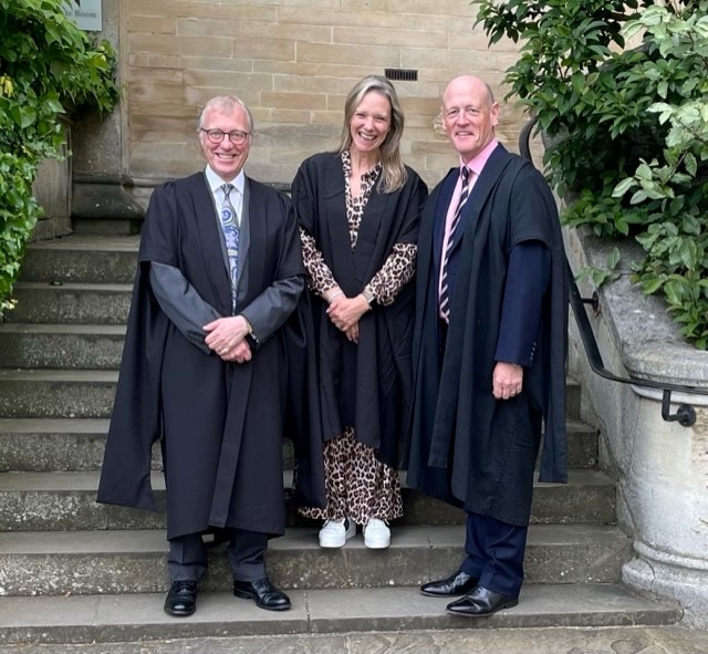 Sir Ernest Ryder, Jane Chesters, and Matthew Kirkby standing on the Hall stairs and smiling.