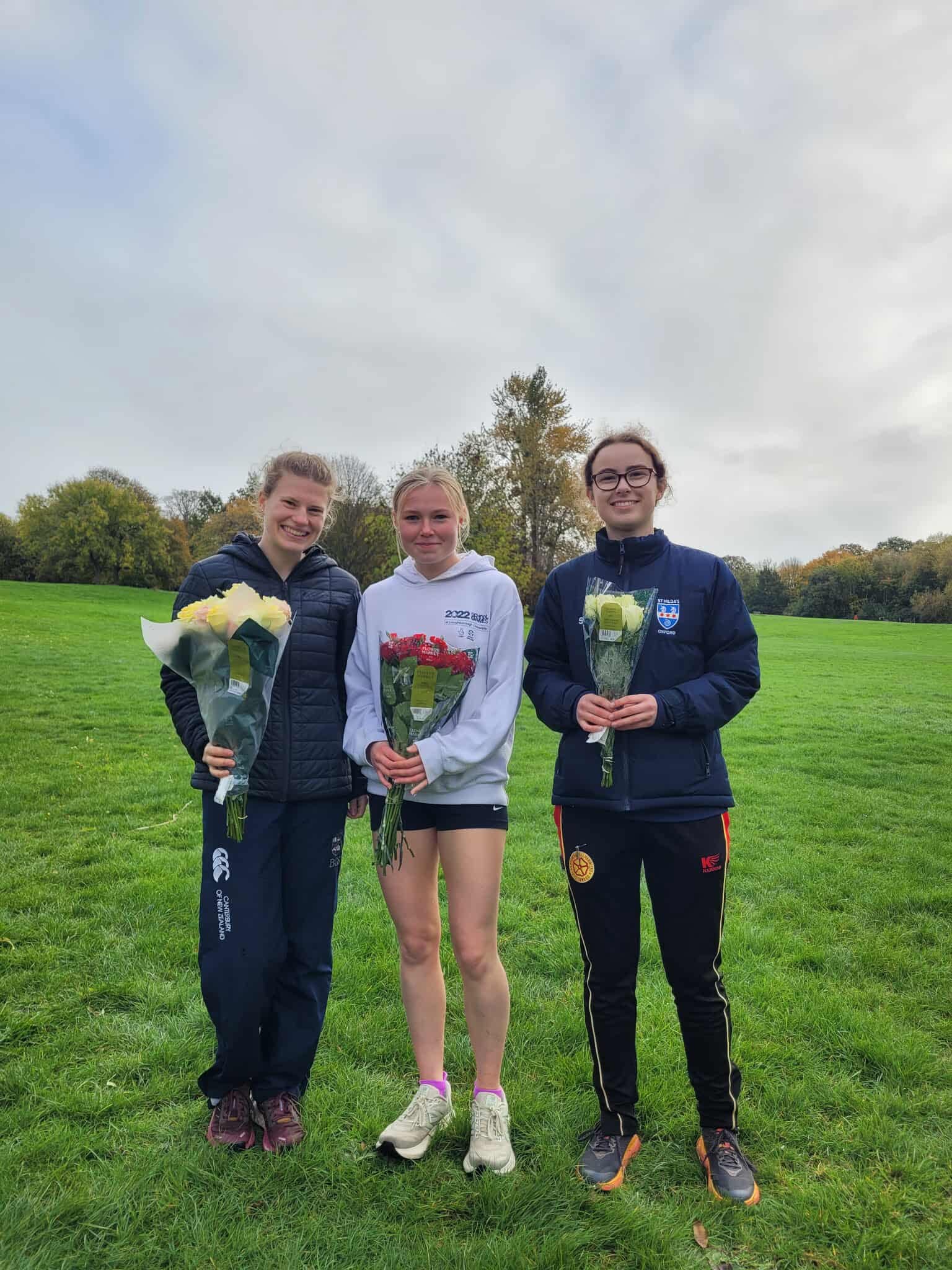 Three women's runners holding flowers at Cross Country Cuppers