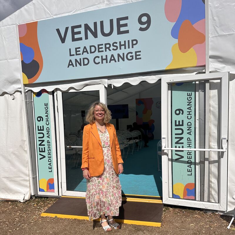 Dyedra Morrissey stood in front of entrance to marquee, with sign above the door reading Venue 9 Leadership and Change