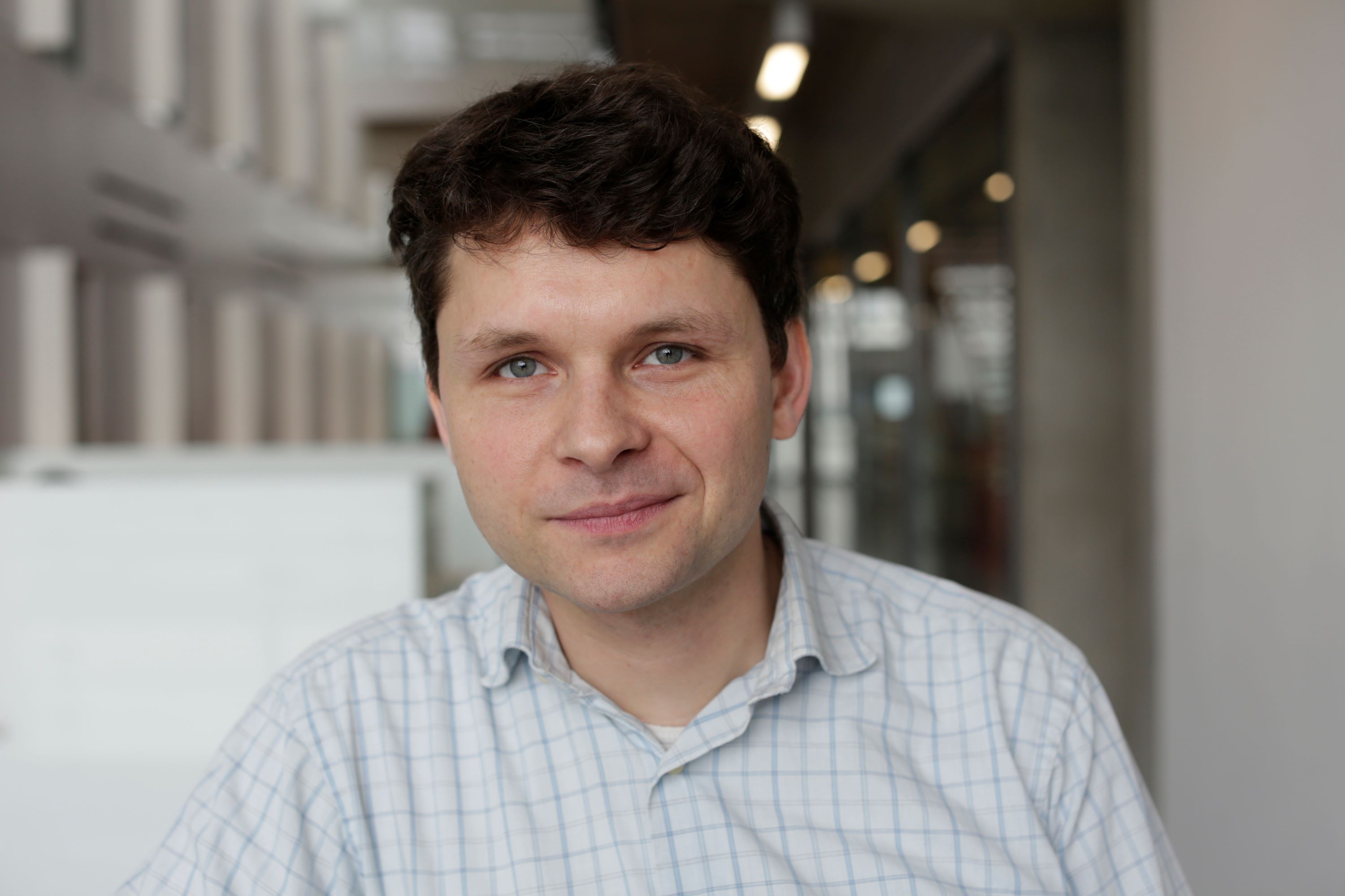 Dr Holger Kramer, with brown hair and blue eyes wearing a white checked shirt, photographed in front of a blurred background.