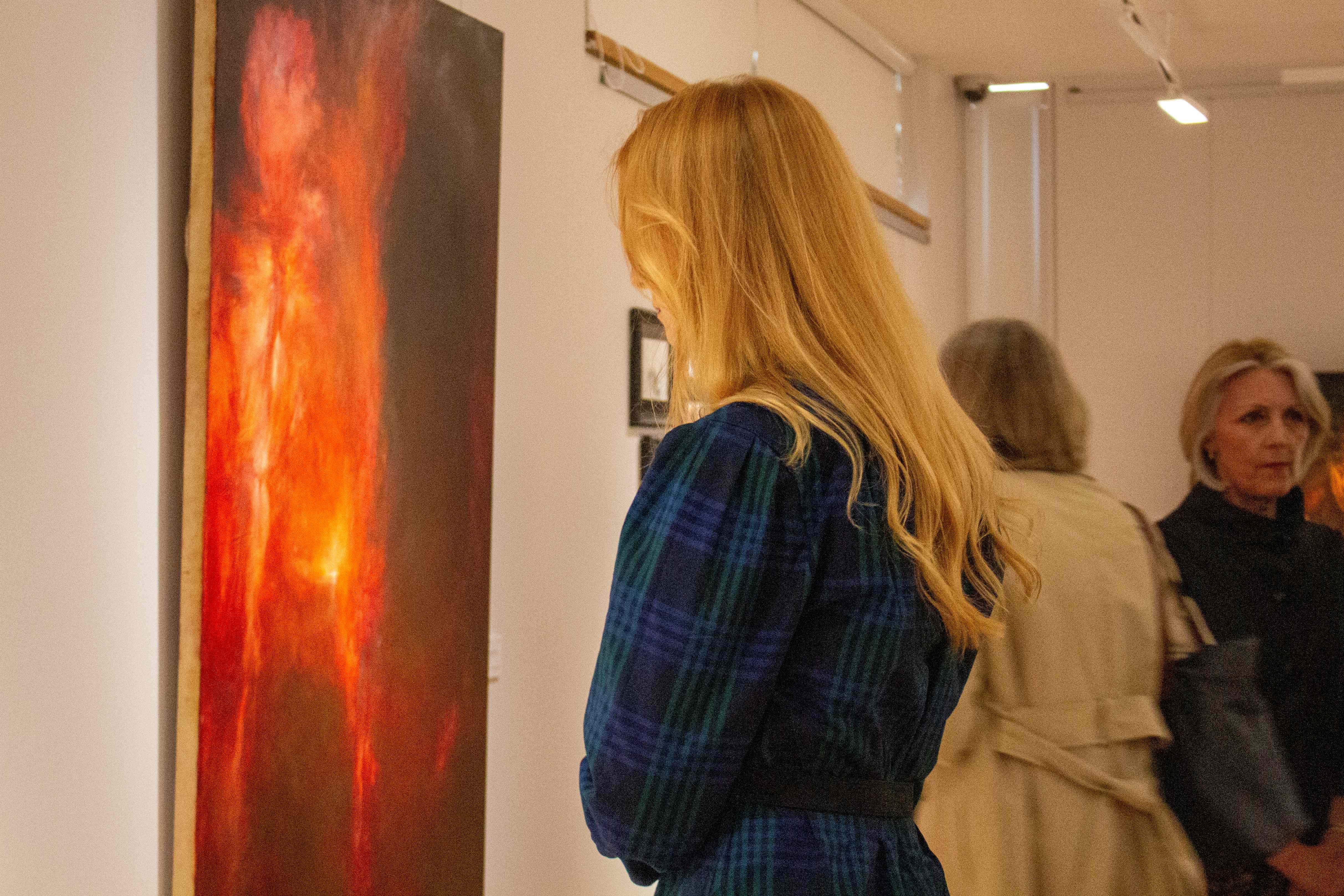 A woman looking at one of Chantal Meza's paintings at the Disappearance of Worlds exhibition.