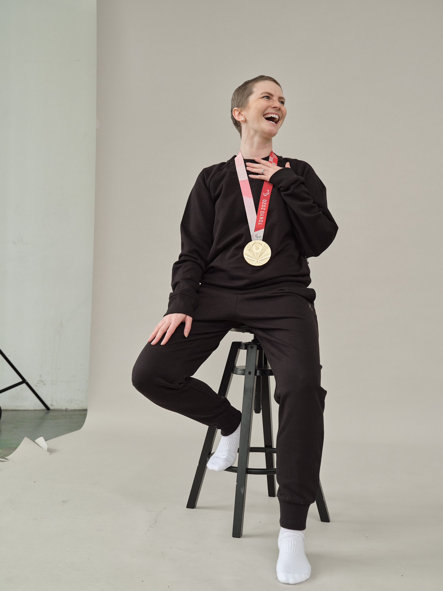 Erin poses seated on a stool with her Paralympic gold medal round her neck, laughing mid-shot.