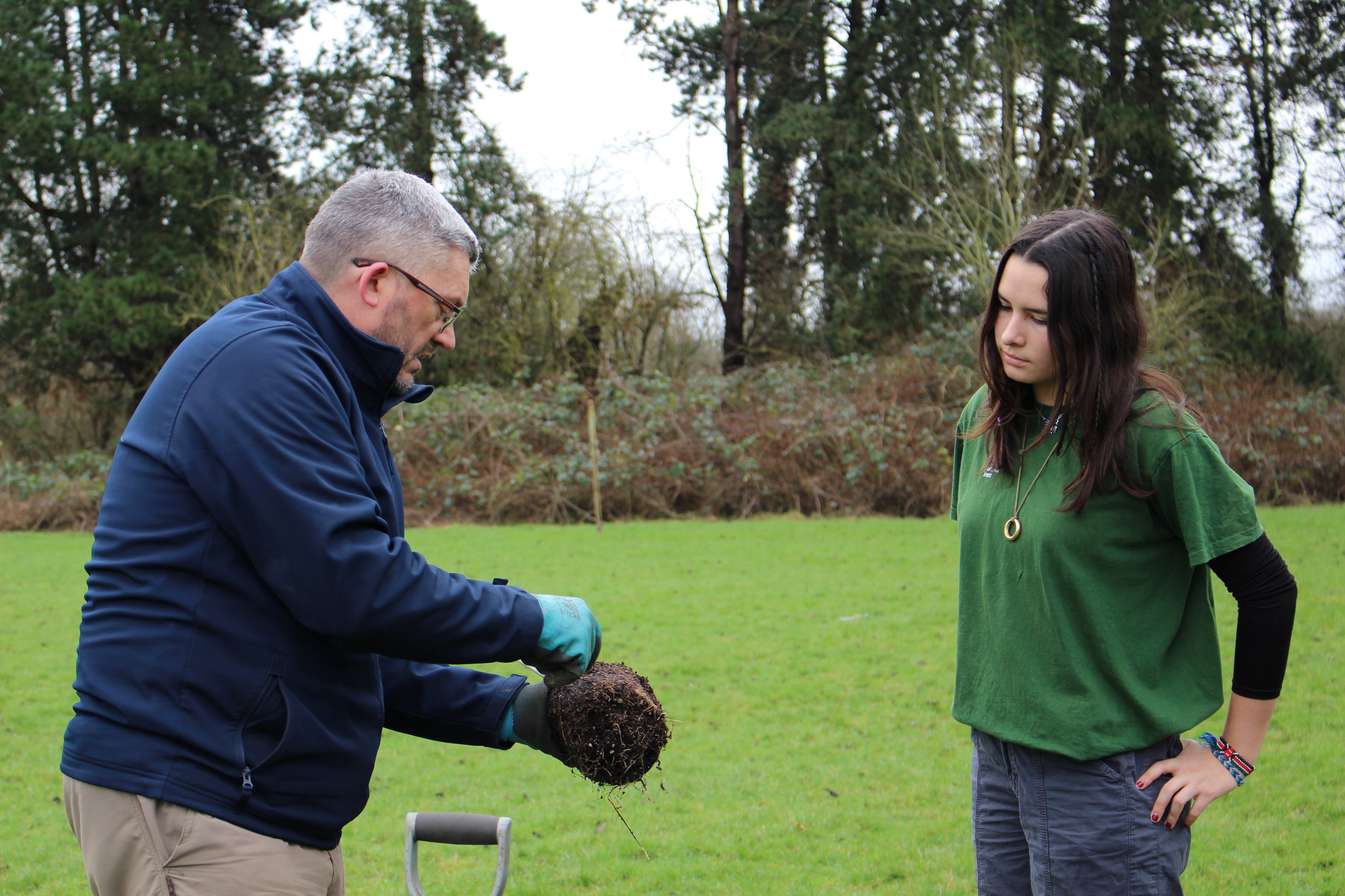 Man holding tree base, showing student how to correctly plant tree
