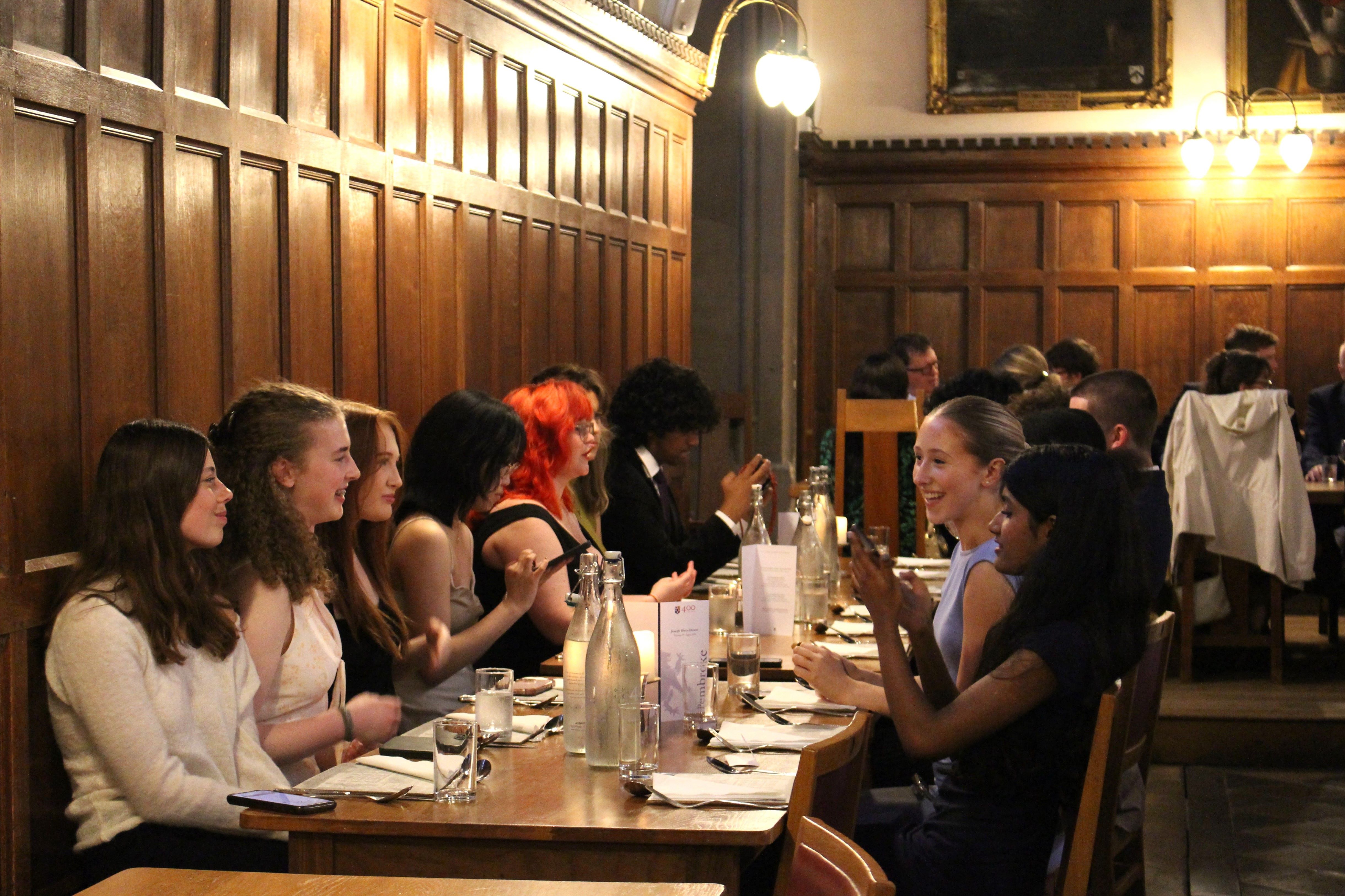 A group of students chatting and laughing whilst sitting in the Dining Hall at Pembroke