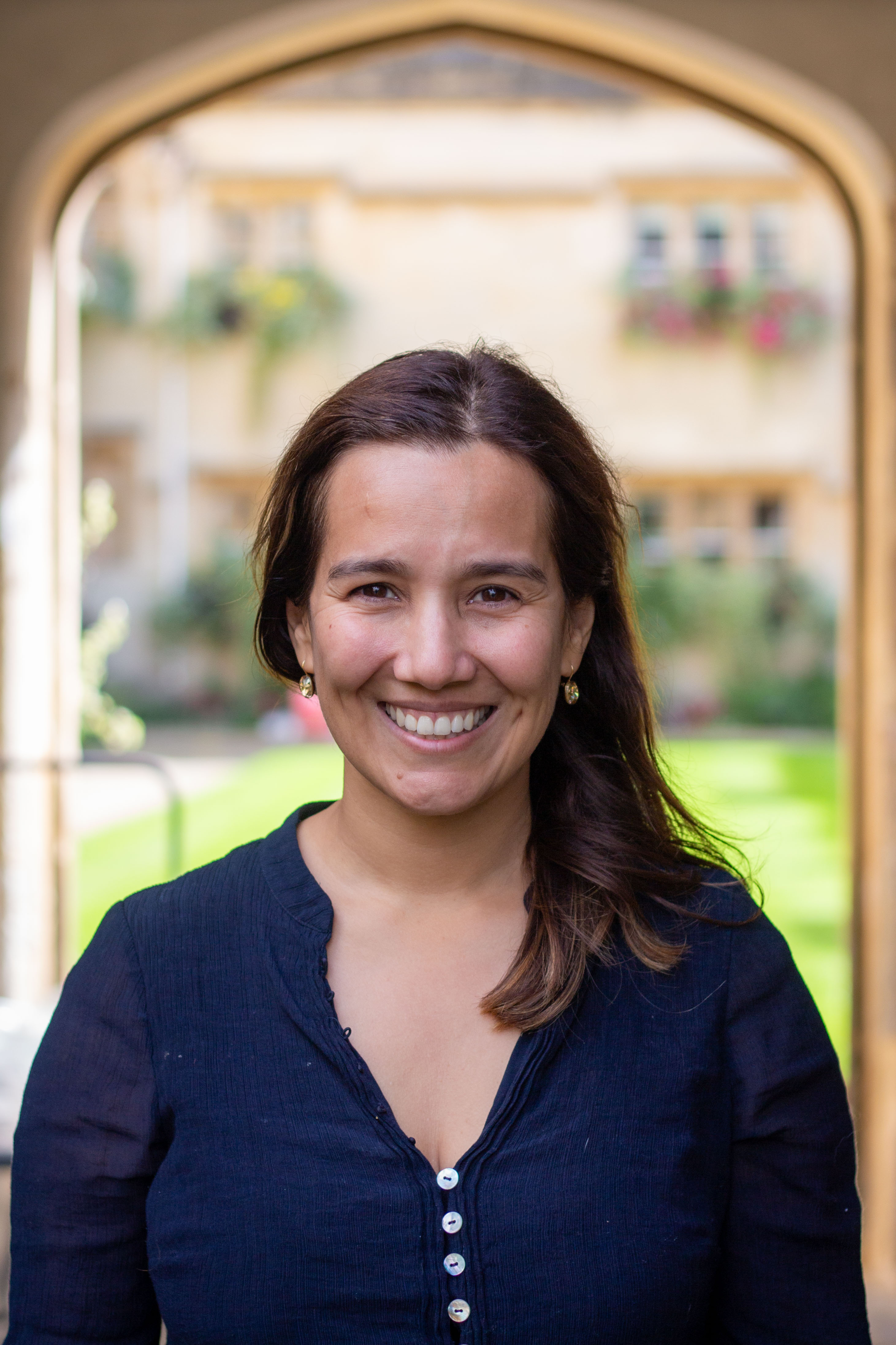 Dr Nicole Miranda smiles at the camera in front of Pembroke's Old Quad.