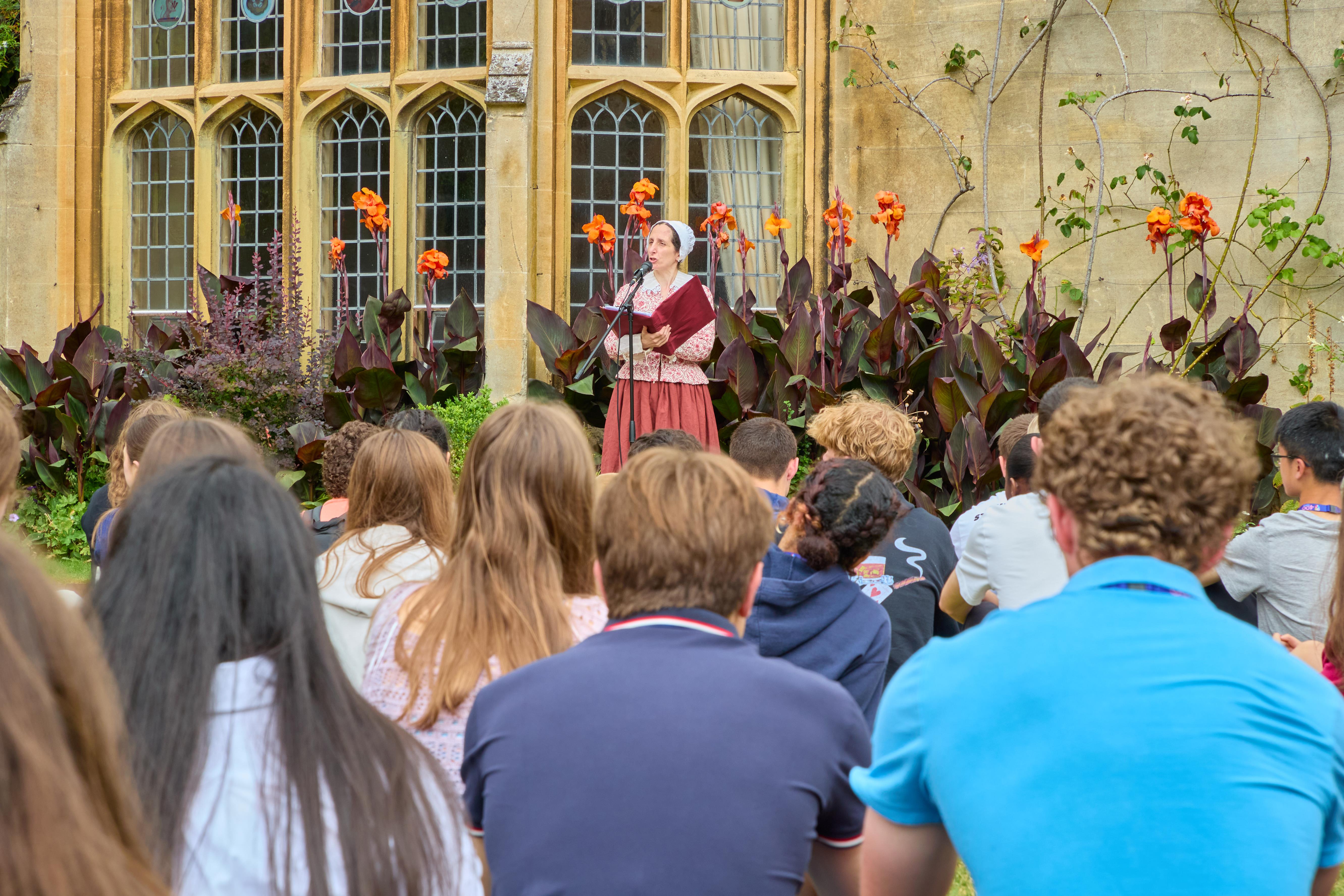 An actress performing an oration for a re-enactment of Pembroke's Foundation Day in front of a group of students