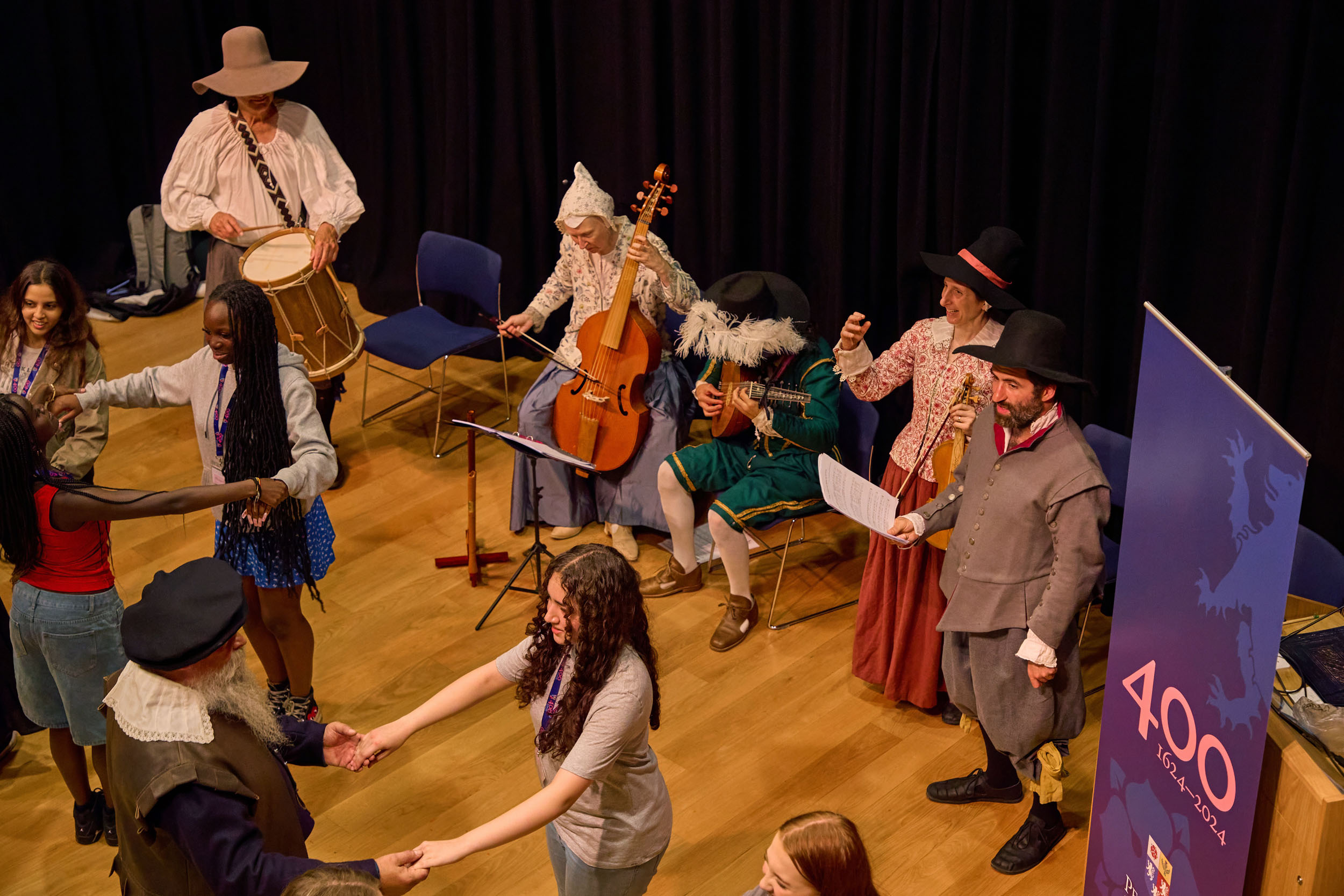 Students take part in 17th century dance, with musicians in period dress in the background.