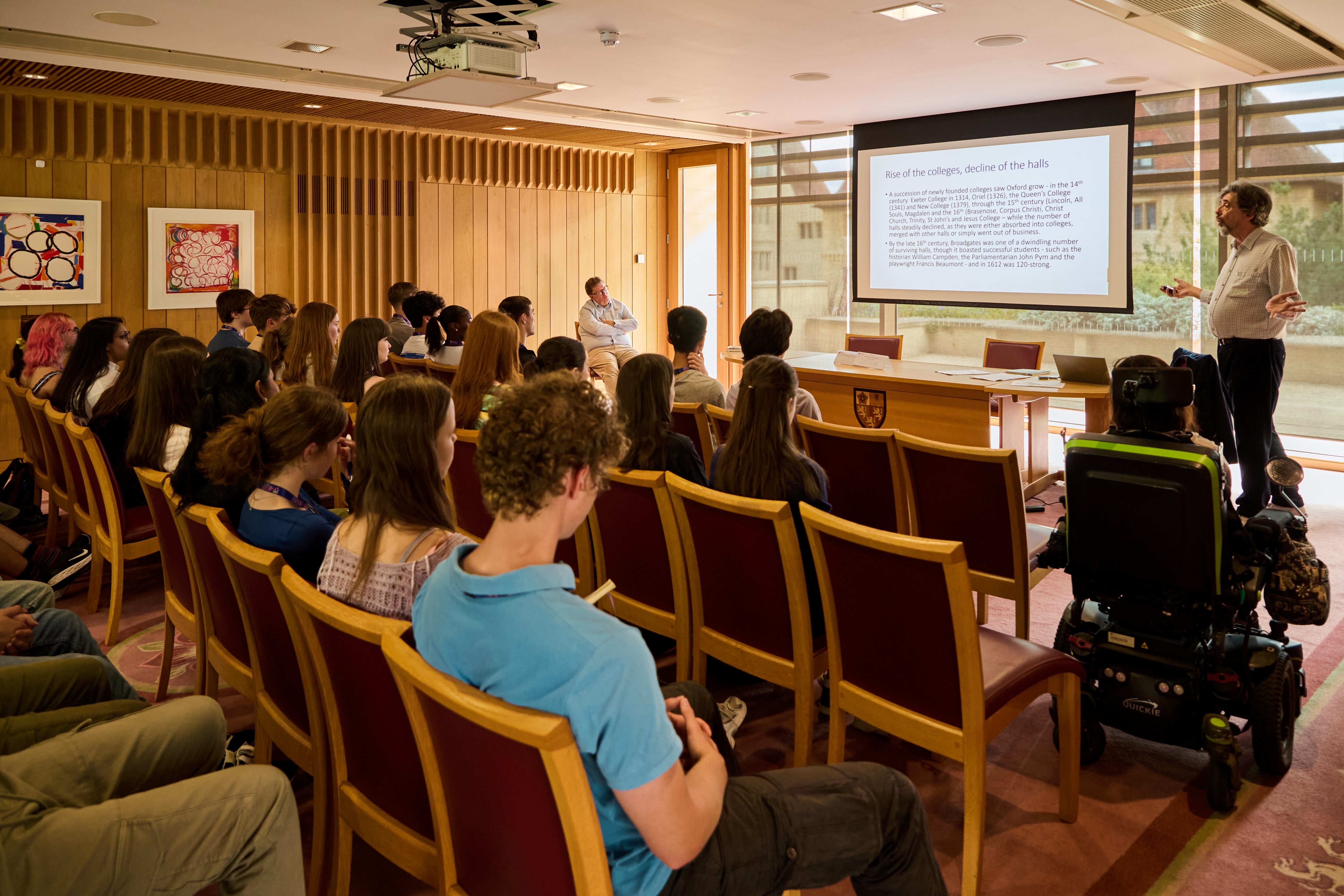 A group of students sat in a lecture room, listening to a presentation made by a tutor