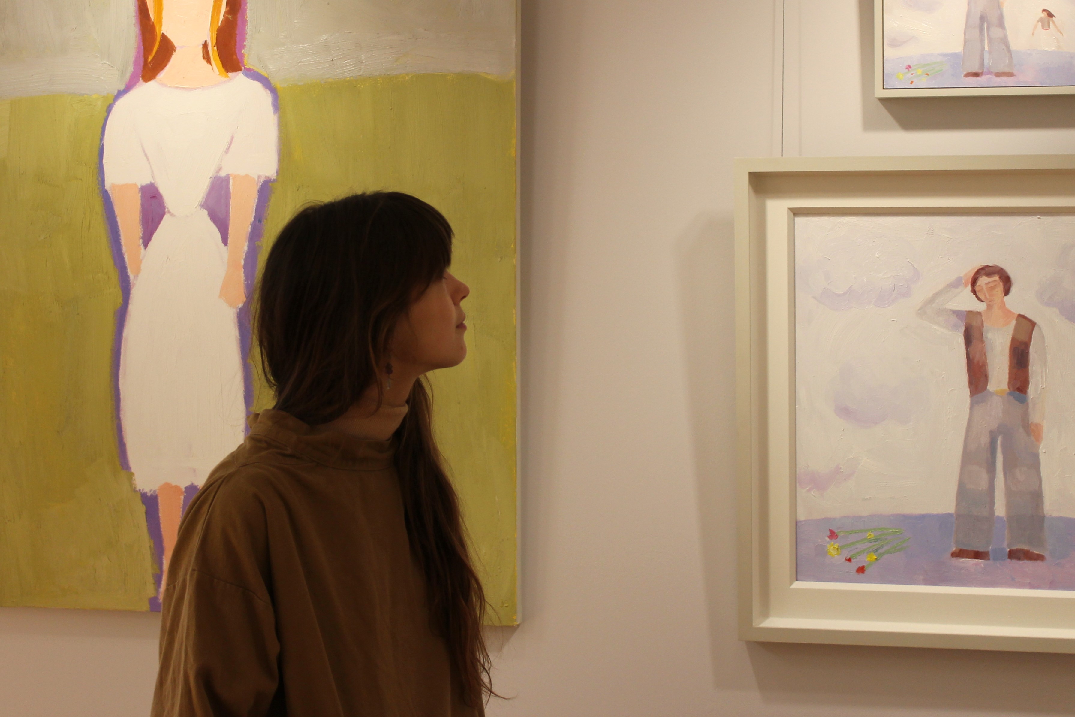 Gabriella Bailey looks at three paintings on the wall. The painting on the left is Julian Bailey's 'Tess' from Tess of the D'Urbervilles, while the right two (identical; one smaller) are Gabriella's, depicting Jude the Obscure.