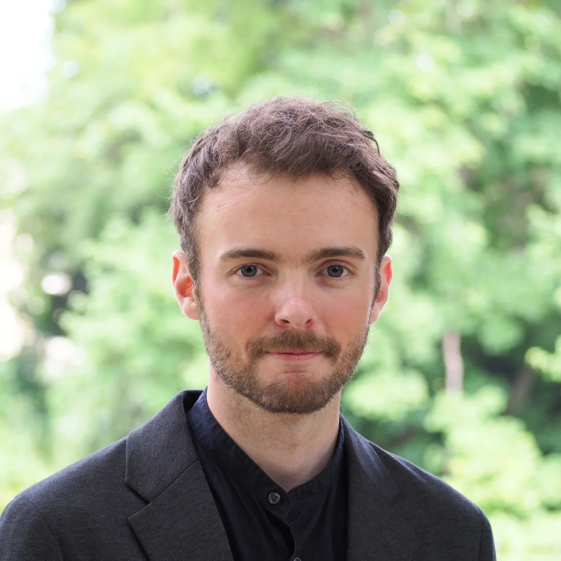 A headshot of Samuel Recht, with blurred green trees in the background.