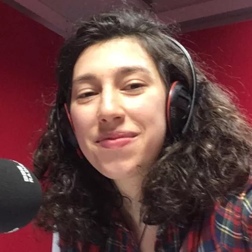 Katerina Johnson photographed in front of a microphone with the BBC logo on it. On the left of the image, there is a Penguin logo.