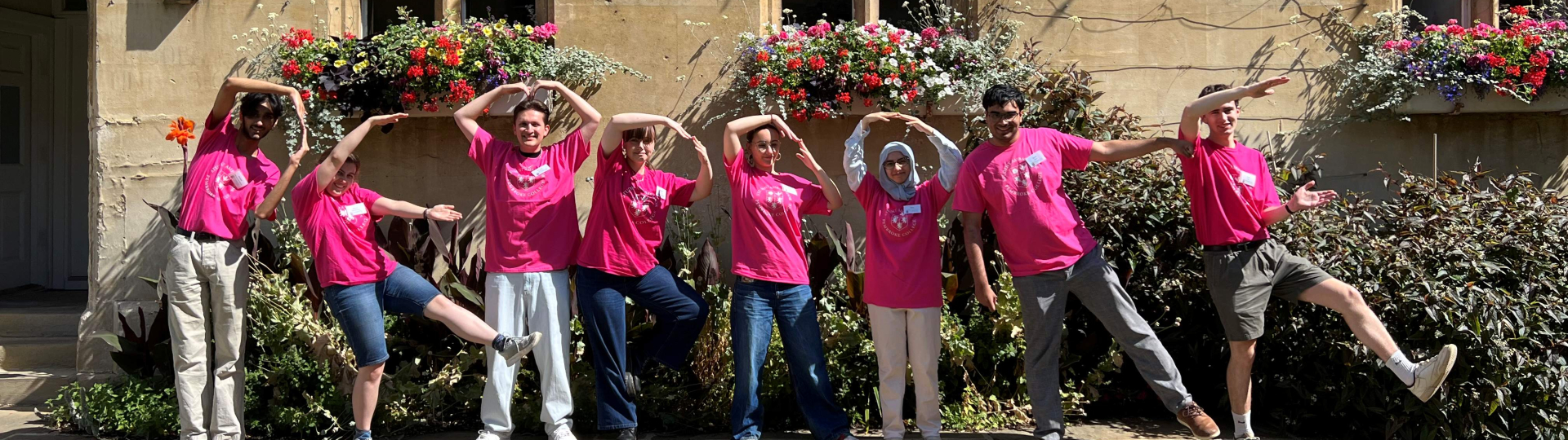 Students stood in a row in front of Old Quad building wearing matching pink tshirts and spelling out 'PEMBROKE' with their bodies