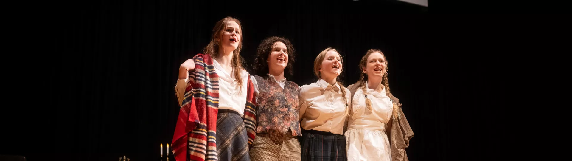 Four students in costume singing together on stage