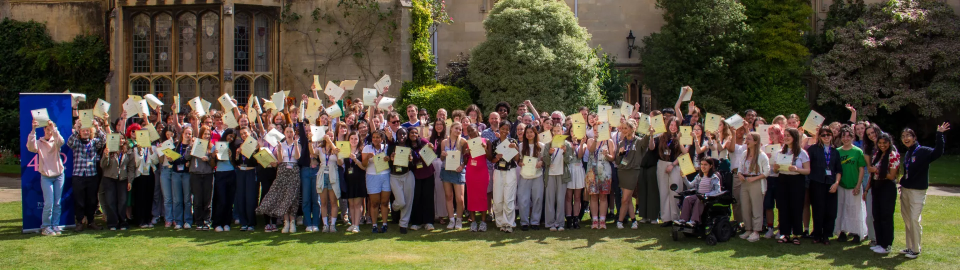 Group of students stood on quad waving certificates