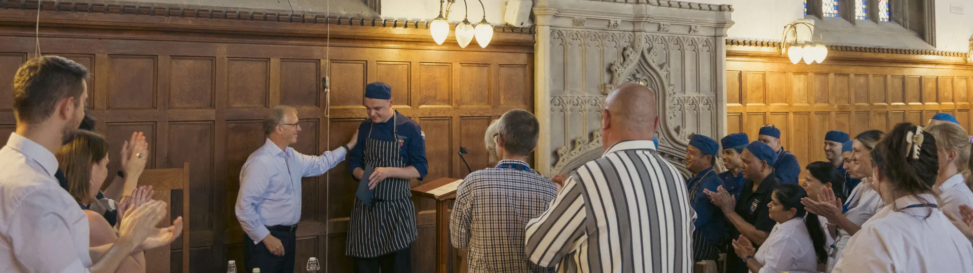 Luke Parsons receiving certificate from Master in Dining Hall with other staff applauding