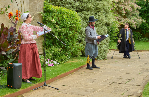 Two performers in 17th century dress read from books in front of Broadgates Hall in Chapel Quad.